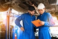 Mechanic in blue work wear uniform inspects the car bottom with his assistant. Automobile repairing service. Royalty Free Stock Photo