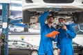 Mechanic in blue work wear uniform inspects the car bottom with his assistant. Automobile repairing service. Royalty Free Stock Photo