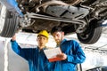 Mechanic in blue work wear uniform inspects the car bottom with his assistant. Automobile repairing service. Royalty Free Stock Photo