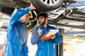 Mechanic in blue work wear uniform inspects the car bottom with his assistant. Automobile repairing service. Royalty Free Stock Photo