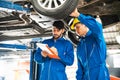 Mechanic in blue work wear uniform inspects the car bottom with his assistant. Automobile repairing service. Royalty Free Stock Photo