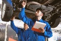 Mechanic in blue work wear uniform inspects the car bottom with his assistant. Automobile repairing service. Royalty Free Stock Photo