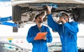 Mechanic in blue work wear uniform inspects the car bottom with his assistant. Automobile repairing service, Royalty Free Stock Photo