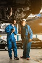 Mechanic in blue work wear uniform inspects the car bottom with a wrench with his assistant. Automobile repairing service. Royalty Free Stock Photo