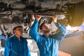 Mechanic in blue work wear uniform inspects the car bottom with a wrench with his assistant. Automobile repairing service. Royalty Free Stock Photo