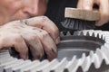 Mechanic with dirty hands cleaning a cog wheel with a steel brush