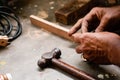 A mechanic does carpenter jobs with wood, plus and other tools. He is hitting hammer on the head of nail to wooden pieces and