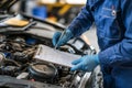 Mechanic examines open car engine while taking notes and inspecting vehicle conditions Royalty Free Stock Photo