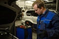 Mechanic in garage checking motor oil level at a car. Car engineer technician in the car repair shop. Automobile maintenance and Royalty Free Stock Photo