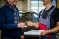 Mechanic givies client keys to his repaired car in a workshop Royalty Free Stock Photo