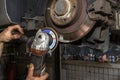 A mechanic grinds, with an angle grinder, the edge of an old rear brake disc in a car, regeneration of the brake system.