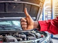 Mechanic hand checking and fixing a broken car in garage.hand of mechanic with thumbs up and tool. Royalty Free Stock Photo