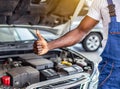 Mechanic hand checking and fixing a broken car in garage.hand of mechanic with thumbs up and tool. Royalty Free Stock Photo