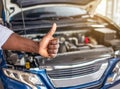 Mechanic hand checking and fixing a broken car in garage.hand of mechanic with thumbs up and tool. Royalty Free Stock Photo