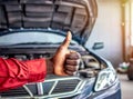 Mechanic hand checking and fixing a broken car in garage.hand of mechanic with thumbs up and tool. Royalty Free Stock Photo