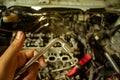 Mechanic hand with a tool of car repair called wrench and service car engine in car garage