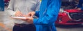 Mechanic holding clipboard with car owner in the workshop garage. Car auto services concepts. Close-up