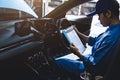 Mechanic holding clipboard and checking inside car to maintenance vehicle by customer claim order in auto repair shop garage. Royalty Free Stock Photo