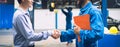 Mechanic holding clipboard shaking hands with car owner in the workshop garage. Car auto services concepts Royalty Free Stock Photo