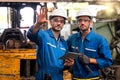 Mechanic holding a wrench and a tablet standing in front of an industrial forklift. Engineers and skilled technicians are looking