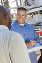 Mechanic Looking At Client While Writing On Clipboard