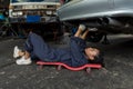 Mechanic lying down and working under car at auto service garage. Technician vehicle maintenance and checking under car at automot
