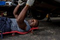 Mechanic lying down and working under car at auto service garage. Technician vehicle maintenance and checking under car at automot Royalty Free Stock Photo