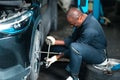Mechanic male staff worker change replace car tire work in garage auto service front wheel
