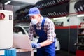 Mechanic man in protective mask with laptop making car diagnostics at service Royalty Free Stock Photo