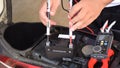 A mechanic is measuring the voltage of a motorcycle battery with clamp meter for maintenance.