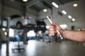 A mechanic in overalls with tools in his hands stands with his arms crossed on his chest.