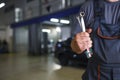 A mechanic in overalls with tools in his hands stands with his arms crossed on his chest.