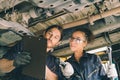 Mechanic service team man and woman working together under car hoist checking list suspension maintenance in garage auto wokshop