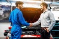 The mechanic shaking hands with customer after finish checking the opened hood red car. Happy mechanic and satisfied customer.