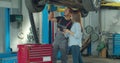 Mechanic teaching woman to repair car. Woman learning and noting or filling in document in garage.