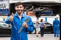 Mechanic thumb up standing and hold a wrench with blur garage in the background. Auto car repair service center.