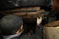 A mechanic unscrews a bolt under a car with a screwdriver to repair a broken part. Repairing a car in a garage in a Royalty Free Stock Photo