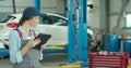 Mechanic woman with tablet walking along car workshop. Car service, repair, maintenance and people concept. Royalty Free Stock Photo