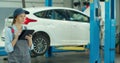 Mechanic woman with tablet walking along car workshop. Car service, repair, maintenance and people concept. Royalty Free Stock Photo