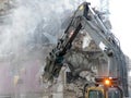 A mechanical digger with a pneumatic hammer tearing down and old building on a an urban development site with dust debris and Royalty Free Stock Photo