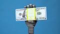 A mechanical hand holds a pack of dollars. A gray cyborg hand holds money on a blue background.