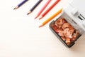 Mechanical sharpener with shavings near colorful pencils on white wooden table, flat lay. Space for text