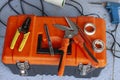 Mechanics placed on the orange plastic toolbox, with cable cutter, cutters, wire stripper and a soldering iron on the floor. Royalty Free Stock Photo