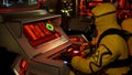 A medic in protective chemical clothing is working at a computer. A man in a yellow bacteriological protective suit and