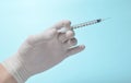 Medic& x27;s hand with white latex gloves holds syringe with needle on blue background. Medical concept. Royalty Free Stock Photo