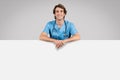 Medical ad. Cheerful male doctor leaning on big blank advertising board with free space for your text, offer or design Royalty Free Stock Photo