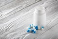 Medical blue pills and white bottle on white wooden background. Royalty Free Stock Photo