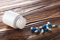 Medical blue pills and white bottle on wooden background. Royalty Free Stock Photo