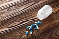 Medical blue pills and white bottle on wooden background. Royalty Free Stock Photo