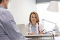 Doctor discussing with mature patient while writing prescription at desk in hospital Royalty Free Stock Photo